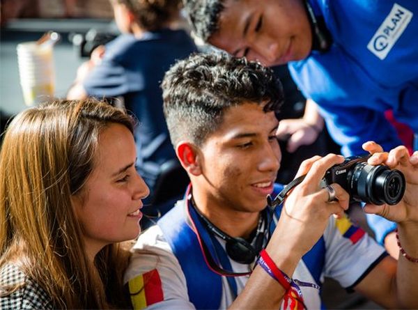 A young woman and two young men look at the display on the back of a Canon camera. © Plan International | Greetje Van Buggenhout